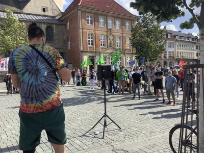 Domplatz Paderborn, Redner im Batik-Look spricht zu Denstrat:innen mit grünen Fahnen